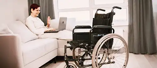 woman sitting on a couch with a laptop with a wheelchair