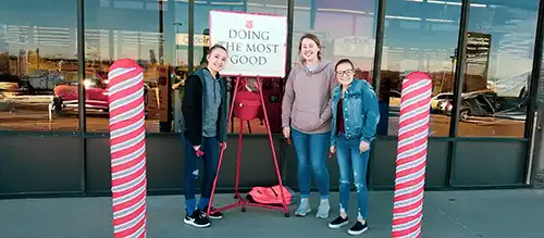 mother and daughters volunteering ringing bell for Salvation Army Christmas donation