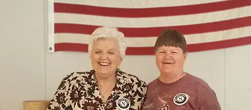 two elderly women smiling in front of an American flag